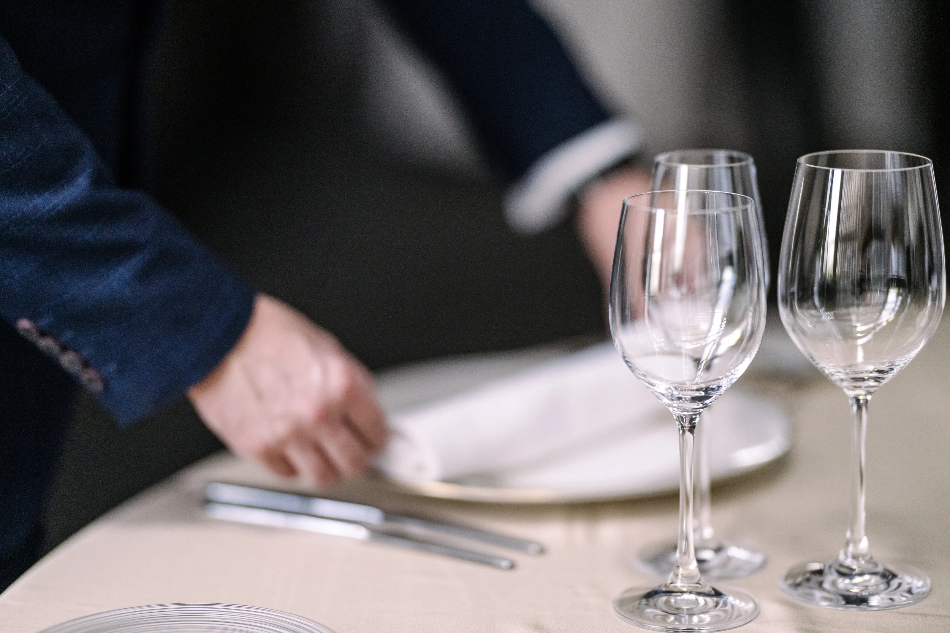 A hand smooths a white napkin beside crystal glasses as the tables are set at Four Seasons Otemachi in Tokyo.