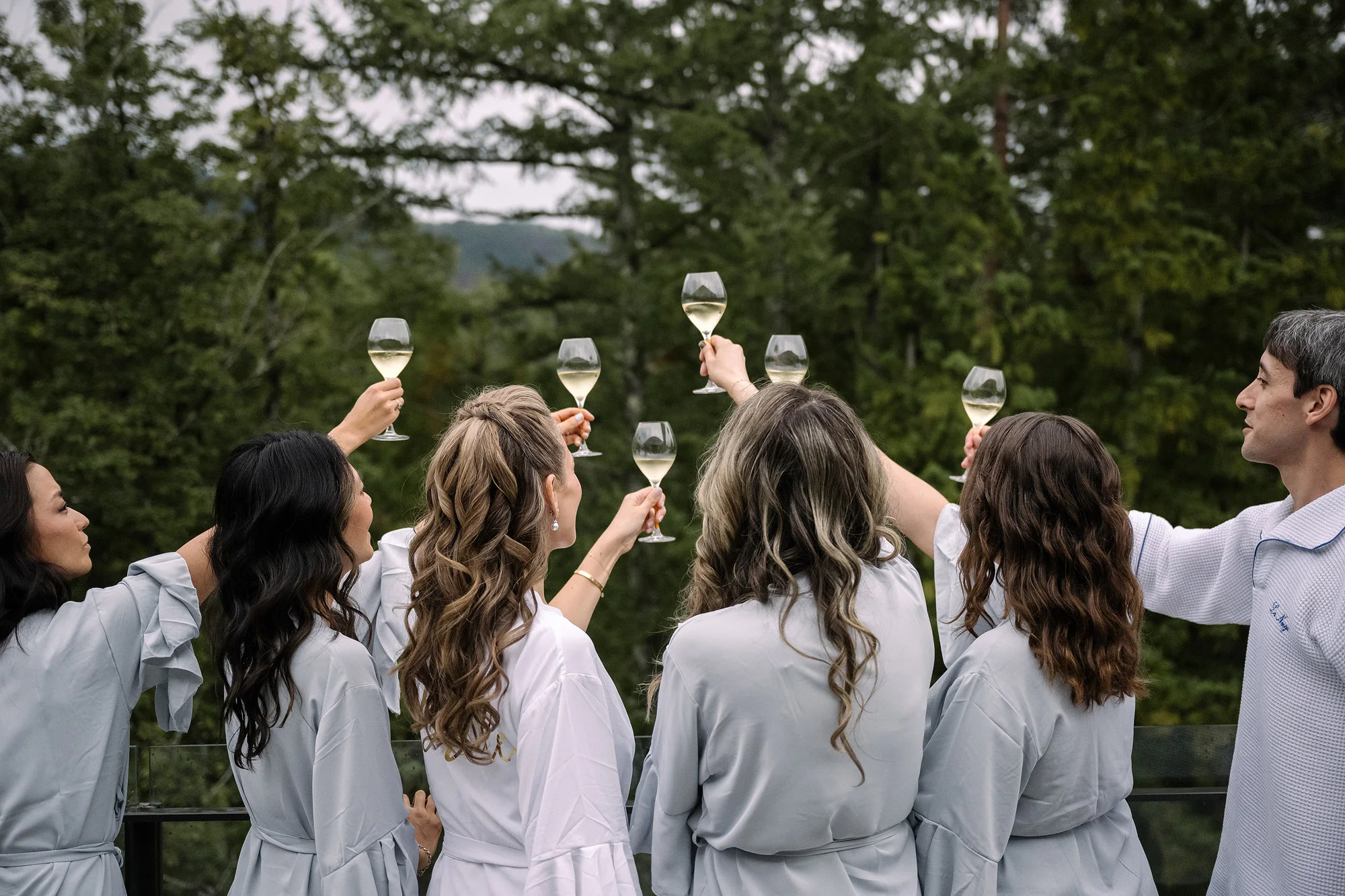 The bride and her bridesmaids in matching robes raise their glasses against a forested mountain view in Hakuba.