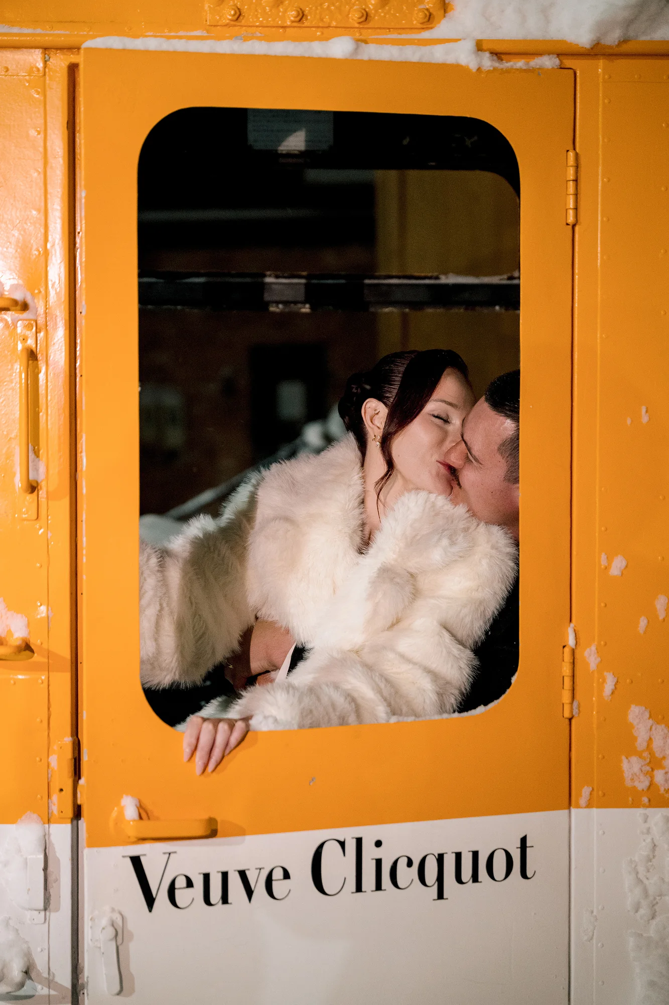 The couple kiss through the window of a vintage yellow gondola in the snow in Hakuba.